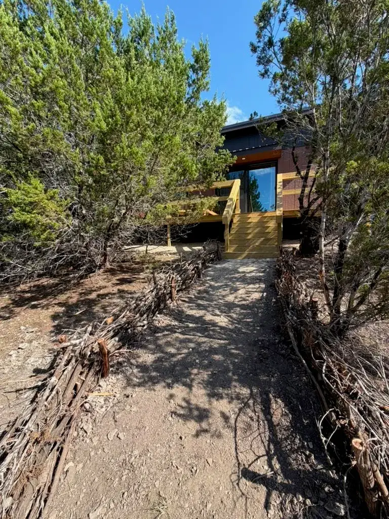 A gravel path between brush fencing, leading to the wooden steps of a casita